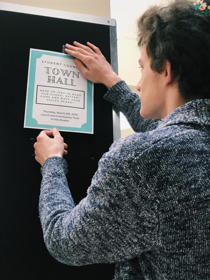 Sophomore class representative Matthew Wieseltier hangs town hall fliers to promote the event.