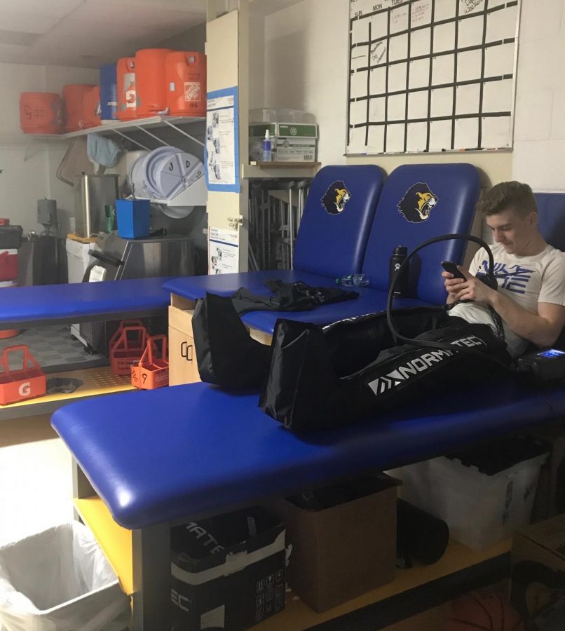CESJDS graduate Dani Offer sits on a table in the training room, where Matula often tapes students’ injuries, using a NormaTec recovery system.