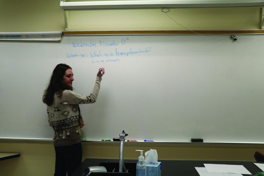 Science teacher Emma Lucore writes down a science warm up for her ninth grade students. Lucore teaches biology.