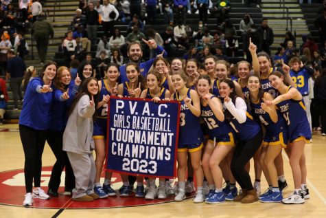 The girls varsity basketball team celebrates their championship banner.